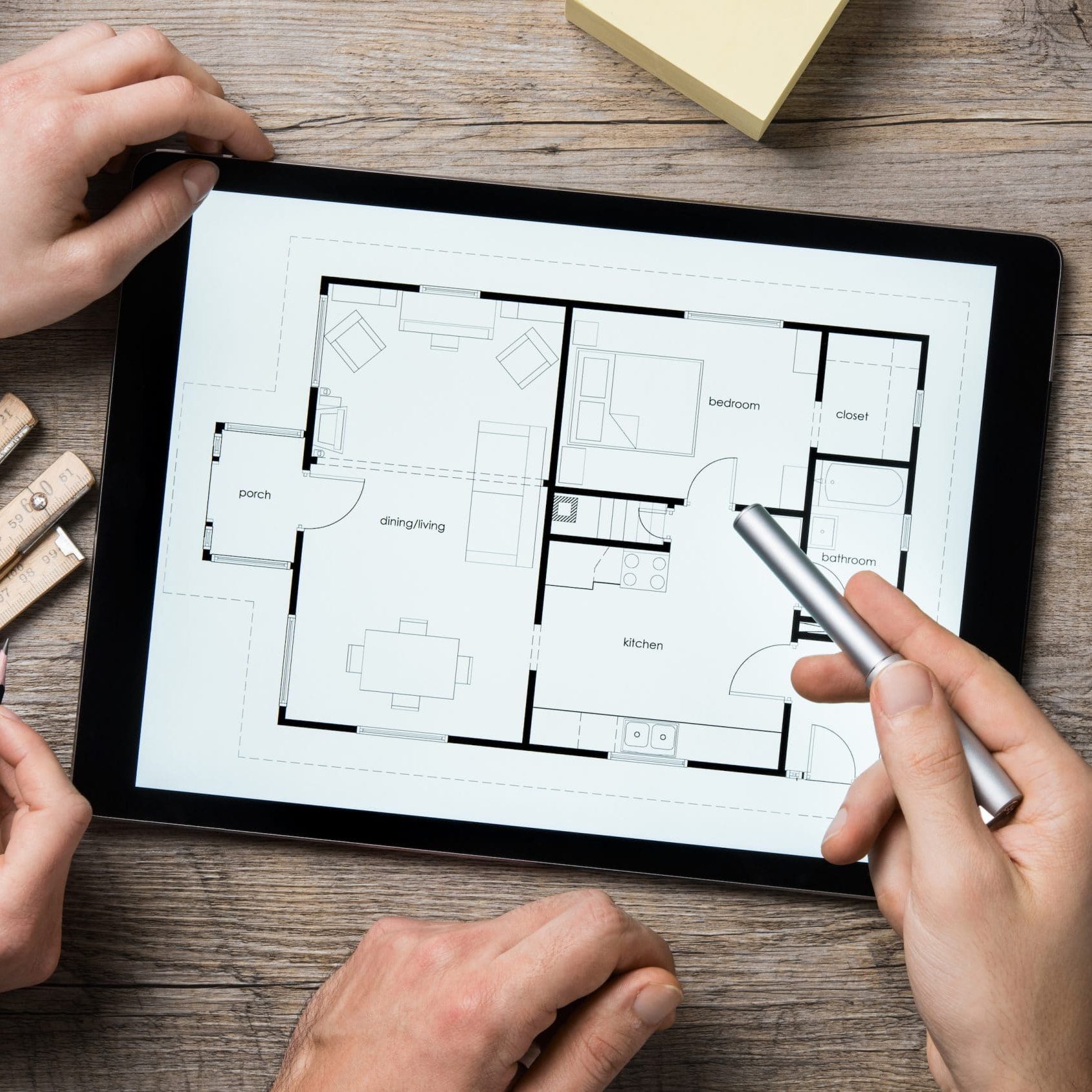 Team of architects working on the house project on a wooden table. Top view of hands pointing architectural project on digital tablet. Interior designer hand working with digital tablet.