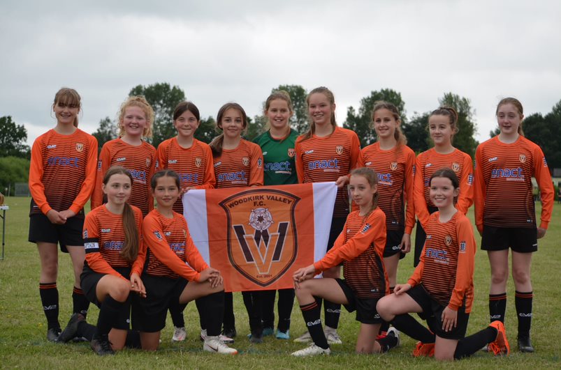 Trophy win for Woodkirk Valley, Girls football team posing with team flag.